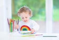 Sweet toddler girl painting rainbow in white room