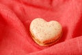Sweet vanilla macaroon macaron in heart shape closeup on pink red textile background. French cookies with raspberry sugar