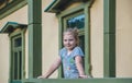 A cute young girl leans on the railing with balusters on the porch of an old building Royalty Free Stock Photo