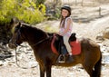 Sweet young girl 7 or 8 years old riding pony horse smiling happy wearing safety jockey helmet in summer holiday Royalty Free Stock Photo