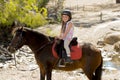 Sweet young girl 7 or 8 years old riding pony horse smiling happy wearing safety jockey helmet in summer holiday Royalty Free Stock Photo