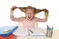 Sweet young little schoolgirl pulling her hair desperate in stress while sitting on school desk doing homework tired Royalty Free Stock Photo