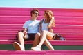 Sweet young loving couple teenagers looking at each other sitting on a pink bench in city park outdoors Royalty Free Stock Photo