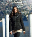 Sweet young woman with winter clothes walking on pier gangway of Lake Lugano with mountains on the background and flare sun light, Royalty Free Stock Photo