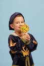 Cute little charming boy in costume of medieval pageboy, little prince with big lollipop over light blue background
