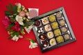 Sweets made of white and dark chocolate in a box decorated with fresh flowers on a red background Royalty Free Stock Photo