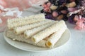 Sweets for tea and coffee on a porcelain plate. Wafer rolls with coconut flakes and cream next to a bouquet of wild field dry