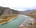 A swift, turbulent turquoise river flows through an autumn valley surrounded by mountain peaks Royalty Free Stock Photo