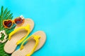 Swimming accessories - sunblock, heart - shaped glasses, yellow flip flop, palm, shells bracelet isolated on blue background Flat