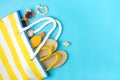 Swimming accessories - trendy beach bag with stripes sunblock, heart - shaped glasses, yellow flip flop, shells on blue background Royalty Free Stock Photo
