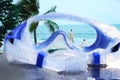 Swimming goggles on beach front and umbrella view sea wave and coconut trees in summer beach holiday concept
