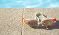 Swimming goggles lie at the edge of the blue pool on a sunny day