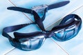 Swimming goggles with water drops on glass on the blue ceramic tiles floor in swimming pool. Professional safety swim goggles