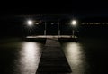 Swimming pier on a lake at night with two lights burning bright over shimmering water and the lights on the opposite shore glowing Royalty Free Stock Photo