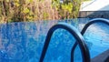 A swimming pool handrail with the reflection if trees on the surface of the swimmming pool