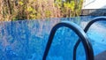 A swimming pool handrail with the reflection if trees on the surface of the swimmming pool Royalty Free Stock Photo