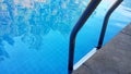 A swimming pool handrail with the reflection if trees on the surface of the swimmming pool Royalty Free Stock Photo