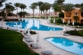 Swimming pool side in resort. Two swimming pools and palms. Empty pool side with closed umbrellas. Hotel buildings around two swim