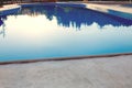 Close-up of a part of swimming pool with a stainless steel ladder and blue water on sunset. Summer vacation, holidays, relax Royalty Free Stock Photo