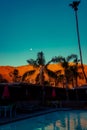 Swimming Pool String Lights and Palm Trees in the Foreground of Red Desert Mountains and Moon at Night Near Palm Springs Royalty Free Stock Photo