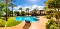 Swimming pool, sun-loungers and palm trees during a warm sunny day, paradise destination for vacations. Backyard swimming pool