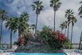 Swimming pool with waterfall and tall palm trees near the ocean under blue partly cloudy sky Royalty Free Stock Photo