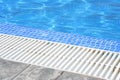 Swimming pool white grating grille with clear blue water and grey tiles.