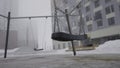 Swing on background of houses in fog. Action. Empty swing eerily seesaw on background of fog. Empty playground in cloudy