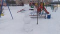 Swings, slides and benches are installed on the playground among residential buildings. A snowman made of snow by children is also