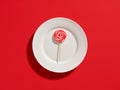 Swirl round candy lollipop on a white plate on red background