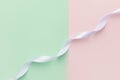 Swirled curly white silk ribbon stretched diagonally on duotone pastel light green pink background. Sewing wedding fashion