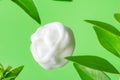Swirled silky white dollop of face cream body lotion on green background with fresh plants leaves. Skin care beauty