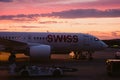 Swiss airline airplane parked in airport during dramatic cloudy summer sunset as seen from inside plane