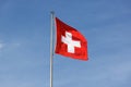swiss flag in the wind in front of a blue sky sunshine during the day. light veil clouds. direct democracy and freedom. sunshine Royalty Free Stock Photo