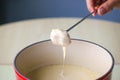 Swiss traditional dish - cheese fondue. Baguette on a fondue fork is being dipped in melted cheese. Served in a communal pot