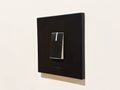 A close-up shot of a modern, square black light switch plate mounted on a plain white or off-white wall Royalty Free Stock Photo