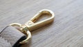 Swivel snap fastener with leather beige bag strap on a wooden background. Metal carabiner with swivel clip or hook. Small gold