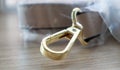 Swivel snap fastener with leather beige bag strap on a wooden background. Metal carabiner with swivel clip or hook. Small gold