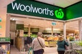 Entrance and exterior view of Woolworths supermarket. Two female customers from behind.