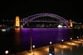 Sydney Harbor Bridge in purple light at night. Glowing water reflection. Embankment promenade. Iconic city waterfront nightscape. Royalty Free Stock Photo