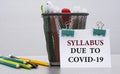 SYLLABUS DUE TO COVID-19 - word on a white sheet with clips against the background of cans of pencils Royalty Free Stock Photo