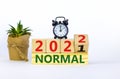 Symbol of covid-19 normal in 2022. Alarm clock. Turned a wooden cube, changed words `normal 2021` to `normal 2022`. Beautiful