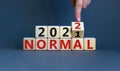 Symbol of covid-19 normal in 2022. Doctor turns a wooden cube and changes words `normal 2021` to `normal 2022`. Beautiful grey