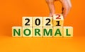 Symbol of covid-19 normal in 2022. Doctor turns a wooden cube and changes words `normal 2021` to `normal 2022`. Beautiful oran