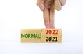 Symbol of covid-19 normal in 2022. Doctor turns a wooden cube and changes words `normal 2021` to `normal 2022`. Beautiful whit