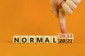 Symbol of covid-19 normal in 2022. Doctor turns wooden cubes and changes words `normal 2021` to `normal 2022`. Beautiful orang