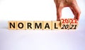 Symbol of covid-19 normal in 2022. Doctor turns wooden cubes and changes words `normal 2021` to `normal 2022`. Beautiful white