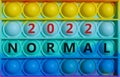 Symbol of covid-19 normal in 2022. Words `Normal 2022` on rainbow Pop It. Beautiful background, copy space. Medical, covid-19