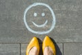 Symbol of happy smiley drawn on the asphalt and woman feet Royalty Free Stock Photo