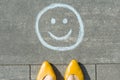 Symbol of happy smiley drawn on the asphalt and woman feet Royalty Free Stock Photo